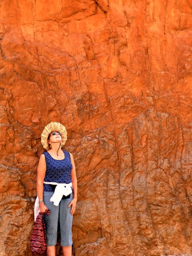 A person standing against the red walls of Standley Chasm looking up to the sun as it comes into view through the narrow aperture above